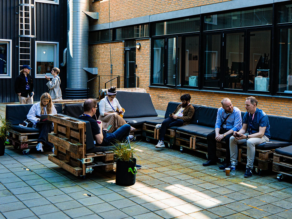Event attendees relax and chat in an outdoor courtyard furnished with modular seating made from stacked pallets and black cushions.
